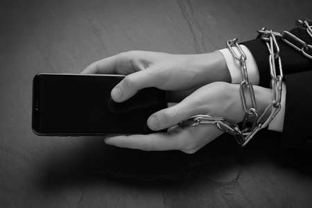 Closeup view of internet addicted woman with chained hands using smartphone at dark table, space for text. black and white effectの写真素材
