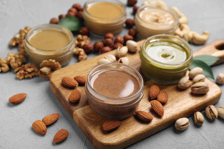 Jars with butters made of different nuts and ingredients on gray table