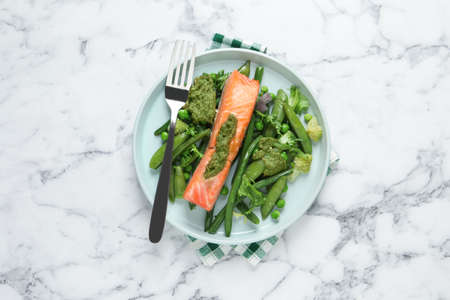 Tasty cooked salmon with pesto sauce and fresh salad served on white marble table, top viewの写真素材