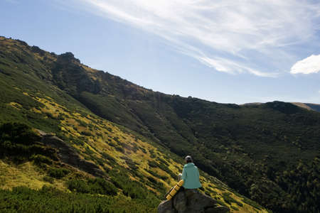 Woman with sleeping mat on rocky cliff in mountains, back viewの写真素材