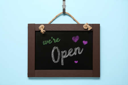 Small chalk board with phrase We're Open on light blue background