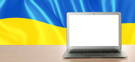 Laptop with blank screen on table and Ukrainian national flag on background, space for text. banner designの写真素材
