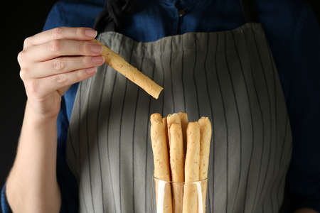 Woman taking fresh delicious grissino from glass on black background, closeup