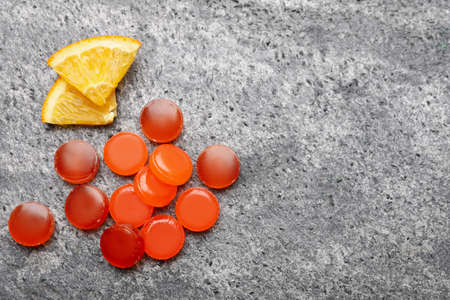 Many cough drops and slices of orange on gray background, flat lay. Space for textの写真素材