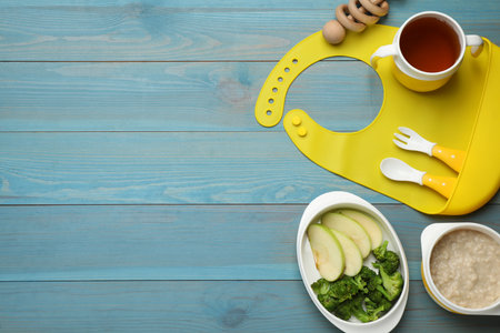 Silicone baby bib, toy and plastic dishware with healthy food on light blue wooden, flat lay. Space for textの写真素材