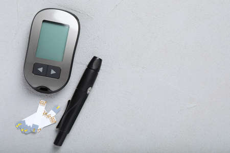 Glucometer, lancet pen and strips on gray table, flat lay with space for text. Diabetes testing kit
