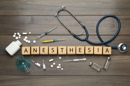 Flat lay composition with word Anesthesia made of cubes and drugs on wooden table