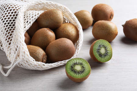 Net bag with cut and whole fresh kiwis on white wooden tableの写真素材
