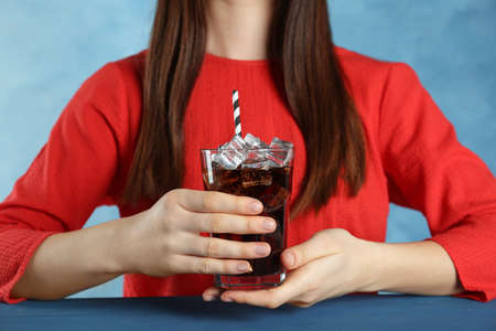 Woman holding glass of cola with ice and straw at blue table, closeup. Refreshing soda waterの写真素材