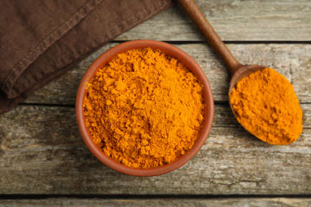 Bowl and spoon with saffron powder on wooden table, flat lay