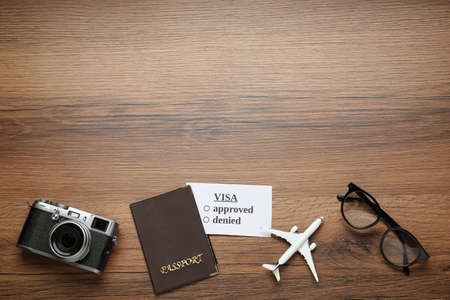 Flat lay composition with passport, toy plane and glasses on wooden table, space for text. Visa...