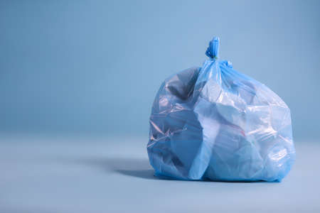 Trash bag full of garbage on light blue background, space for textの写真素材