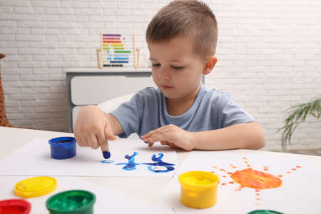 Little boy painting with finger at white table in roomの写真素材