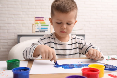 Little boy painting with finger at wooden table in roomの写真素材