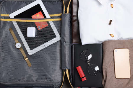 Open suitcase with folded clothes and accessories, closeup. Packing for business trip