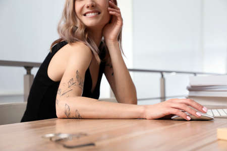 Beautiful woman with tattoos on arms using computer at table indoors, closeupの写真素材