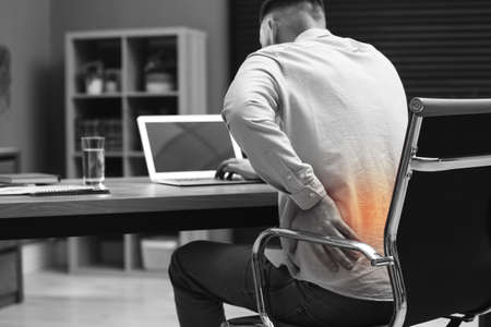 Man suffering from back pain while working with laptop in office. Symptom of poor postureの写真素材
