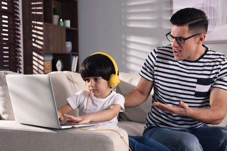 internet addiction. Man scolding his son while he using laptop in living room