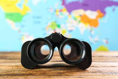 Modern binoculars on wooden table against blurred map