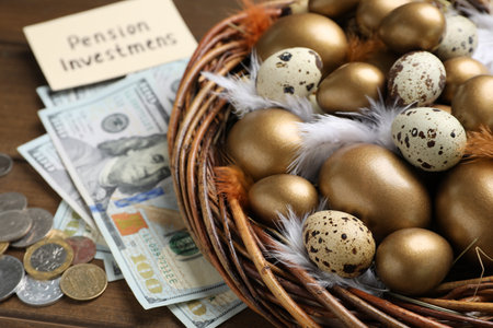 Money, card with phrase Pension Investments near many golden and quail eggs in nest on wooden tableの写真素材