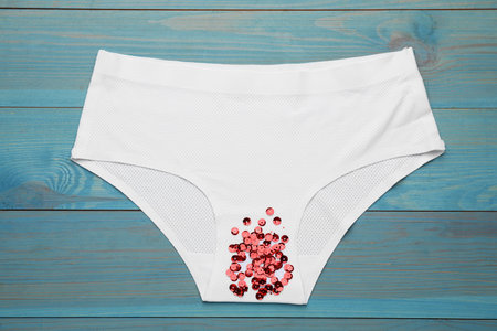 Woman's panties with red sequins on turquoise wooden background, top view. menstrual cycleの写真素材