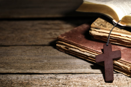Wooden Christian cross and old books on table, closeup. Space for textの写真素材