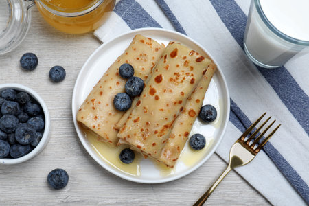 Delicious crepes served with blueberries, honey and milk on white wooden table, flat layの写真素材