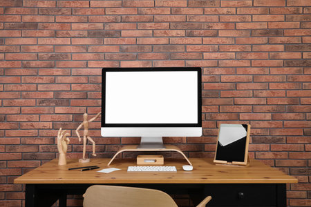 Modern computer and tablet with blank screens on desk near brick wall, space for design. Comfortable workplaceの写真素材