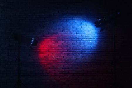 Bright blue and red spotlights near brick wall in dark room, space for textの写真素材