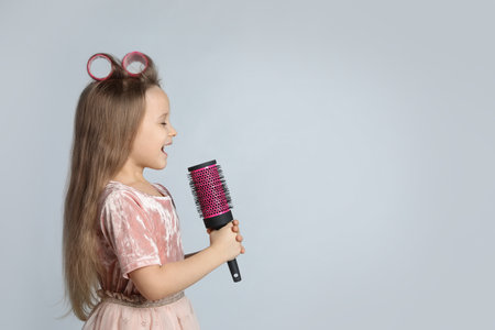 Cute little girl with hairbrush singing on light gray background, space for textの写真素材