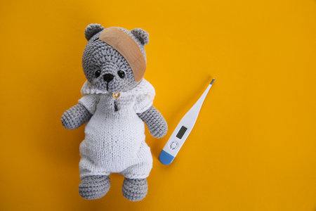 Cute toy bear with sticking plaster and thermometer on orange background, flat lay. children's...