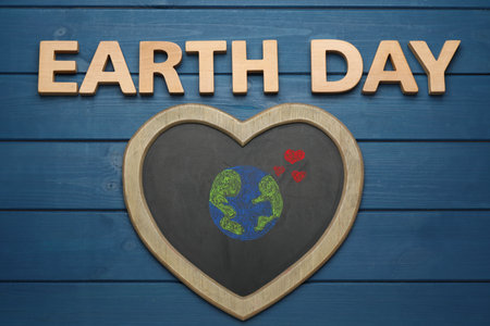 Words Earth Day and heart shaped blackboard with planet drawing on blue wooden table, flat layの写真素材