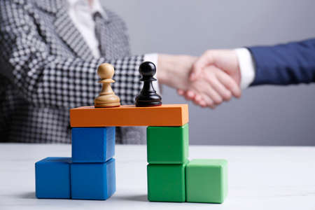 Businesspeople shaking hands against gray background, focus on bridge made of colorful blocks with...