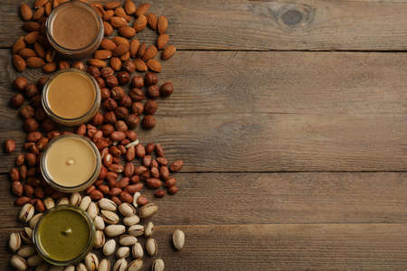 Jars with butters made of different nuts and ingredients on wooden table, flat lay. Space for textの写真素材