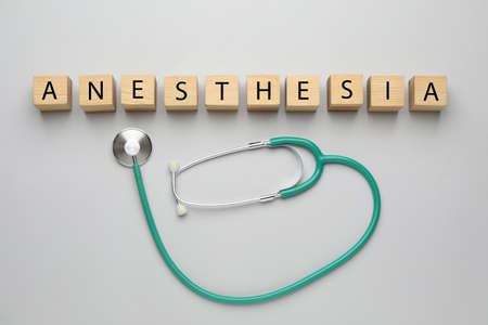 Wooden cubes with word Anesthesia and stethoscope on light gray background, flat lay
