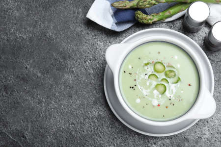 Bowl of delicious asparagus soup on gray table, flat lay. Space for textの写真素材