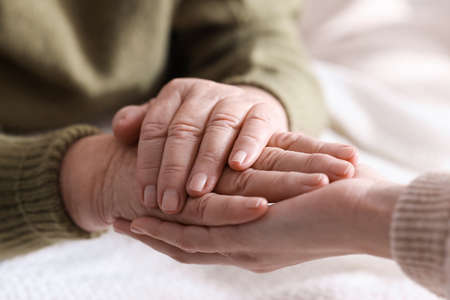 Young and elderly women holding hands together indoors, closeup