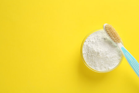 Bowl of tooth powder and brush on yellow background, flat lay. Space for textの写真素材