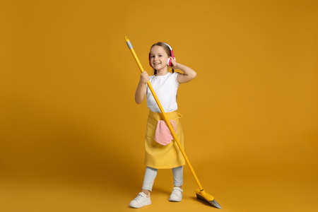 Cute little girl in headphones with broom on orange backgroundの写真素材