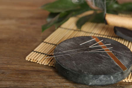 Gray stone coaster with acupuncture needles on wooden table. Space for textの写真素材