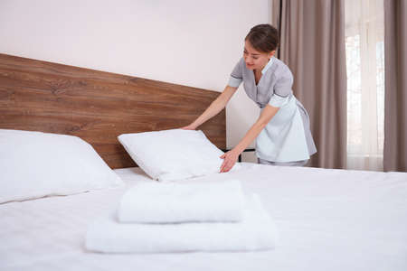 Beautiful chambermaid making bed in hotel roomの写真素材