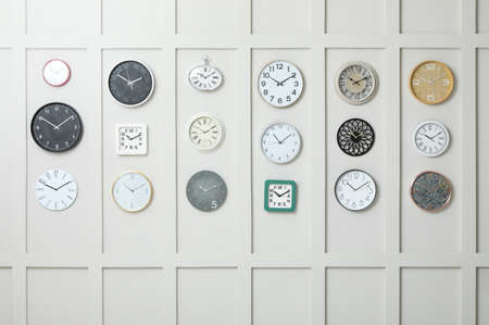 Many different clocks hanging on white wall.
