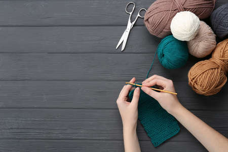 Woman crocheting with teal thread at gray wooden table, top view. Space for text