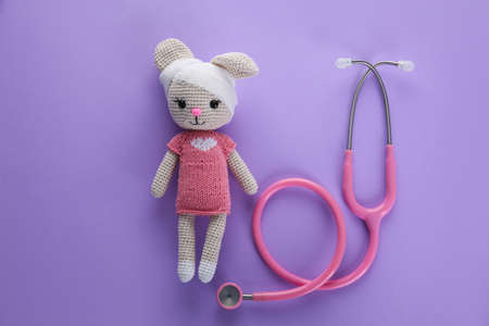 Cute toy bunny with bandage and stethoscope on violet background, flat lay. children's hospitalの写真素材