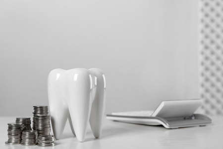 Ceramic model of tooth, coins and calculator on white table, space for text. Expensive treatmentの写真素材