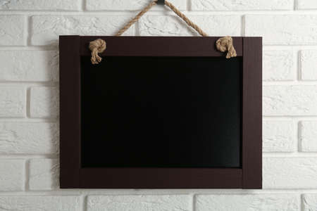 Clean small black chalkboard hanging on white brick wall