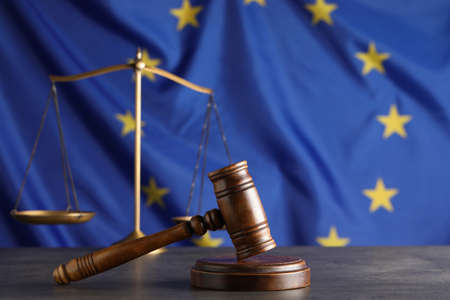 Wooden judge's gavel and Scales of justice on gray table against European Union flagの写真素材