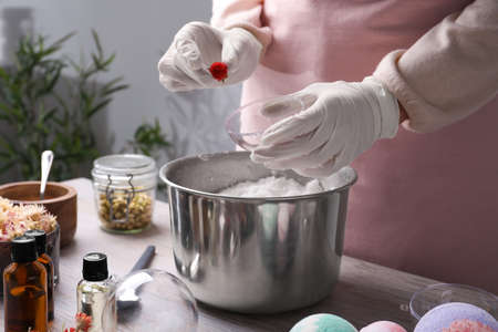 Woman in gloves putting dried flower into bath bomb mold at wooden table indoors, closeupの写真素材