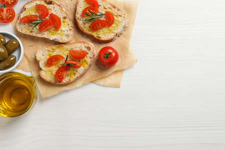 Tasty bruschettas with oil, tomatoes and rosemary on white wooden table, flat lay. Space for textの写真素材