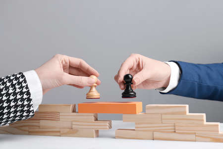 Businesspeople putting pawns on bridge made of wooden blocks at table, closeup. Connection, relationships and deal conceptの写真素材